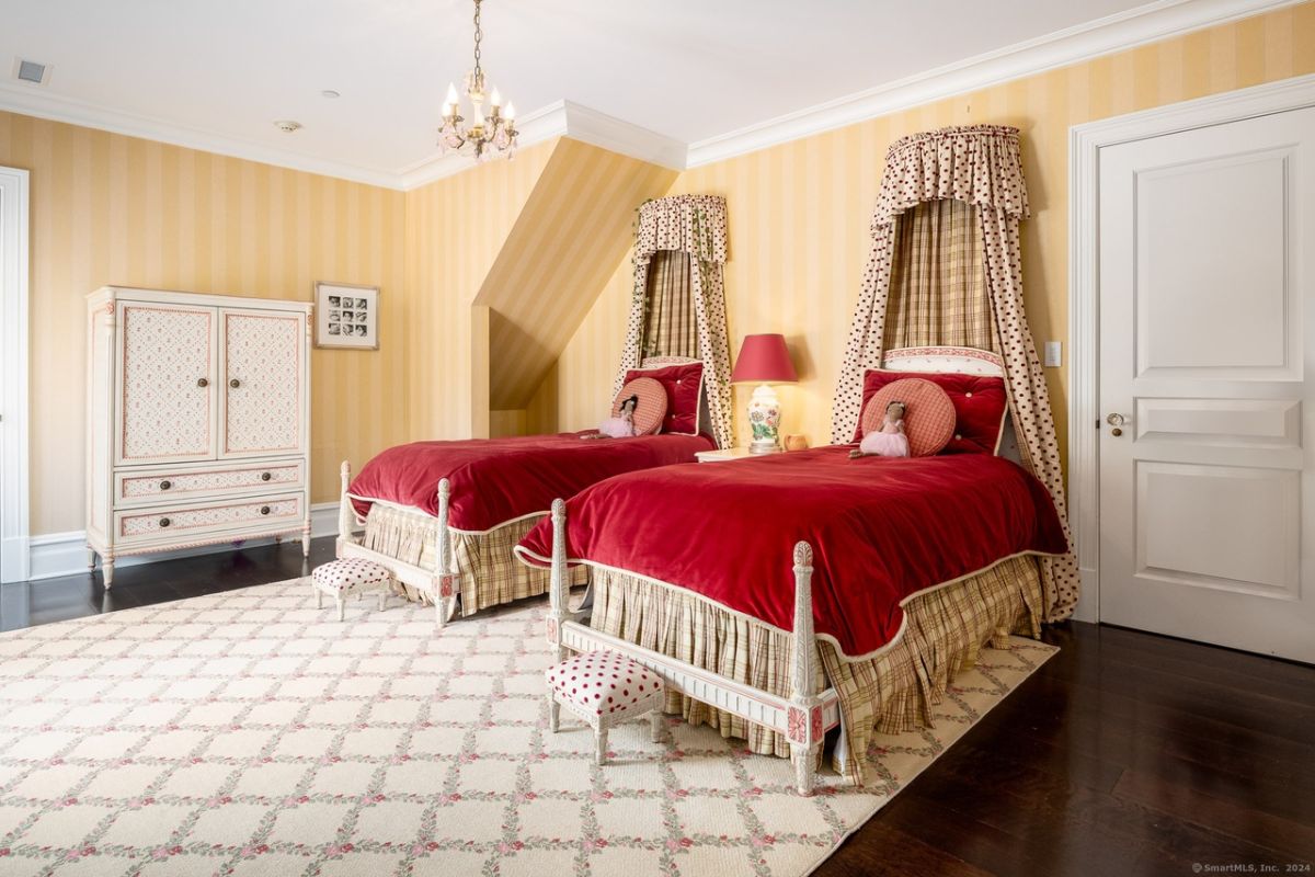 A bedroom with two beds, wallpaper, a rug, and a cabinet.