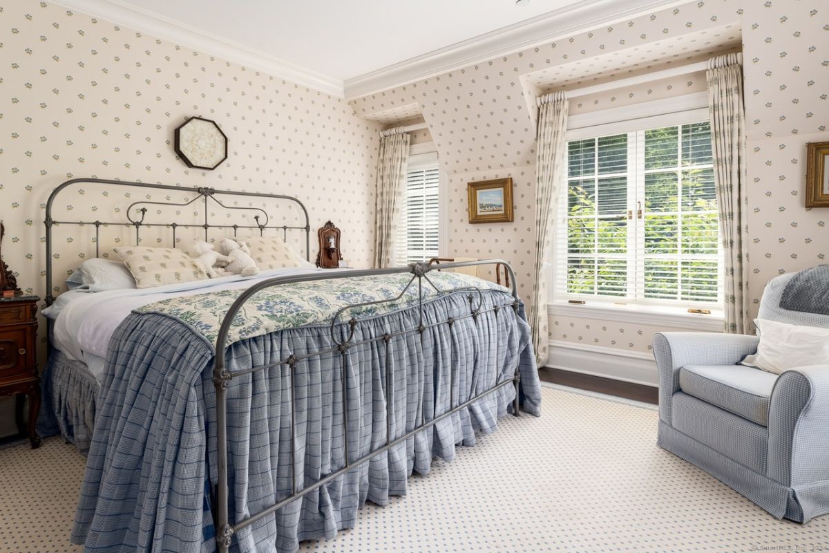 A bedroom with a bed, nightstand, wallpaper, windows, and a studio couch.