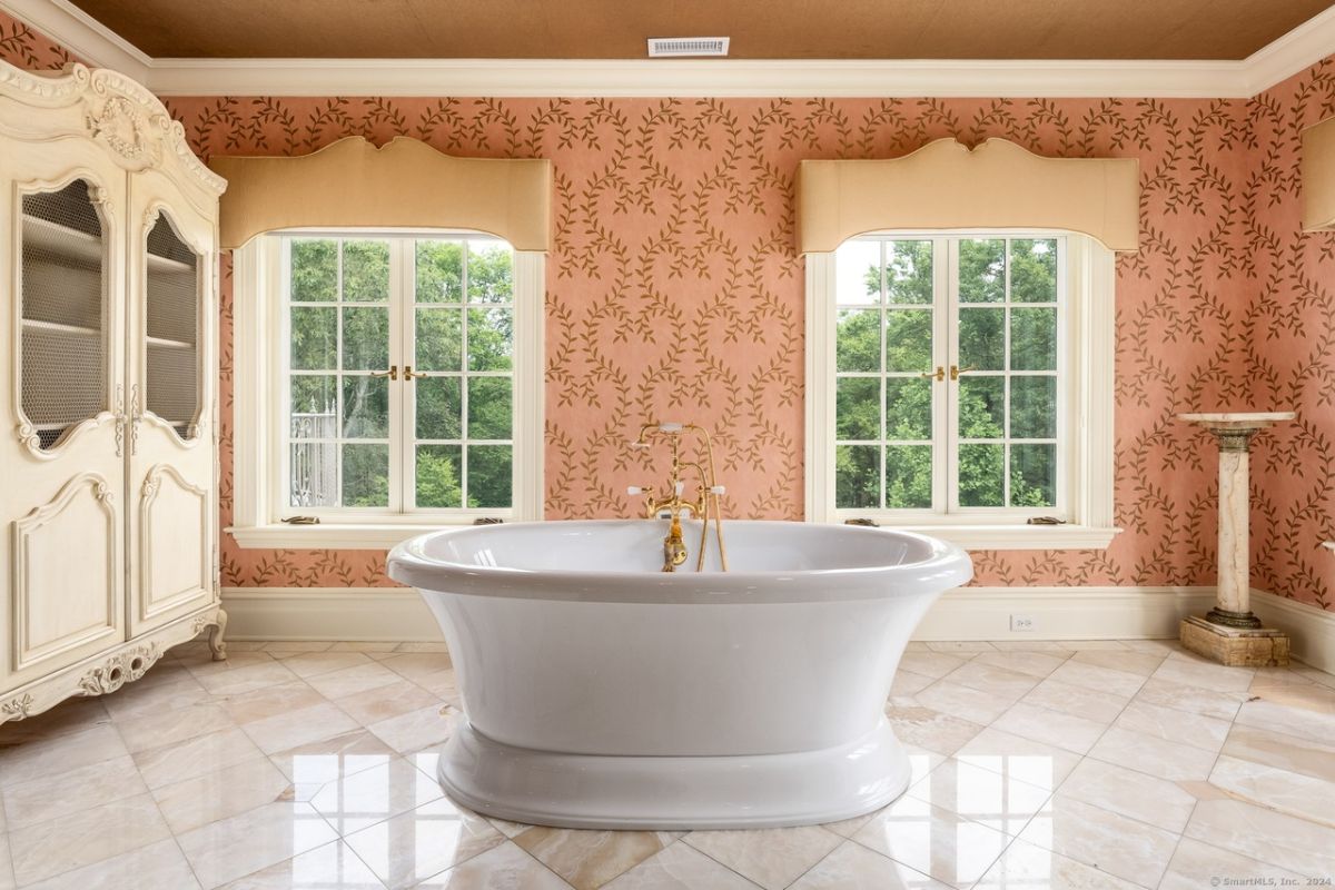 A bathroom with windows, wallpaper, a tiled floor, and a bathtub.