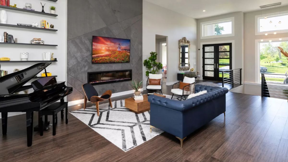 A living room with a shelf, TV, fireplace, piano, rug, chairs, and couch.