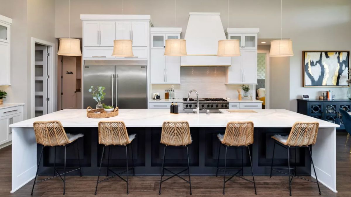 A kitchen with countertops, stools, sink, cabinets, and kitchen appliances.