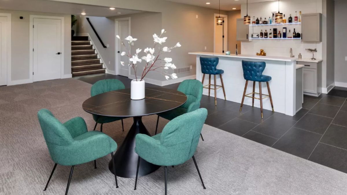 A bar with a countertop, shelf, stools, and a round table surrounded by chairs.