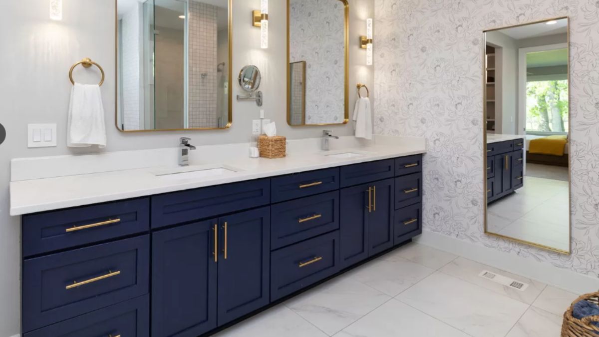 A bathroom with wallpaper, mirrors, a vanity, and cabinets.