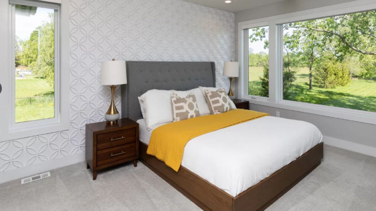 A bedroom with wallpaper, windows, a nightstand, and a bed with a headboard.