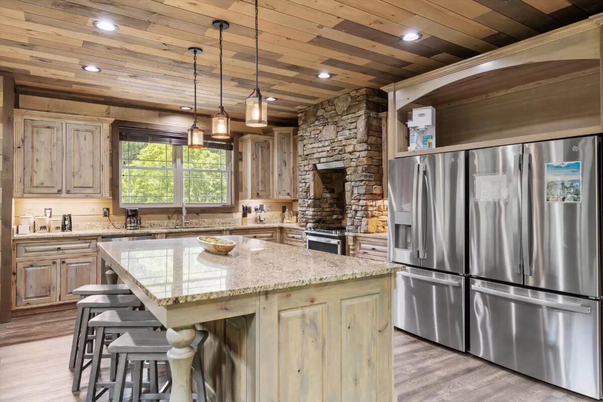 Kitchen with wooden cabinets, two fridges, and a breakfast island under a wood-paneled ceiling.