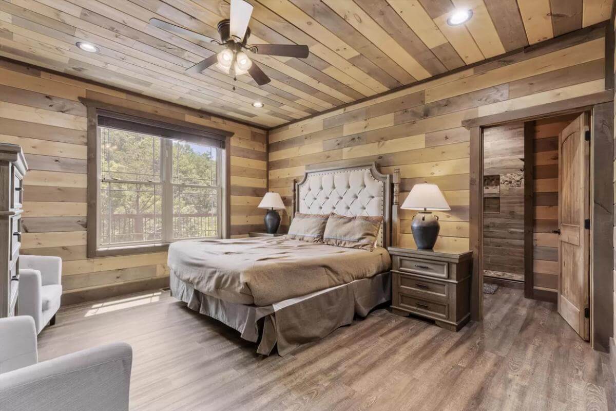 Primary bedroom with a tufted bed, upholstered chairs, and wood-paneled walls echoed on the ceiling.