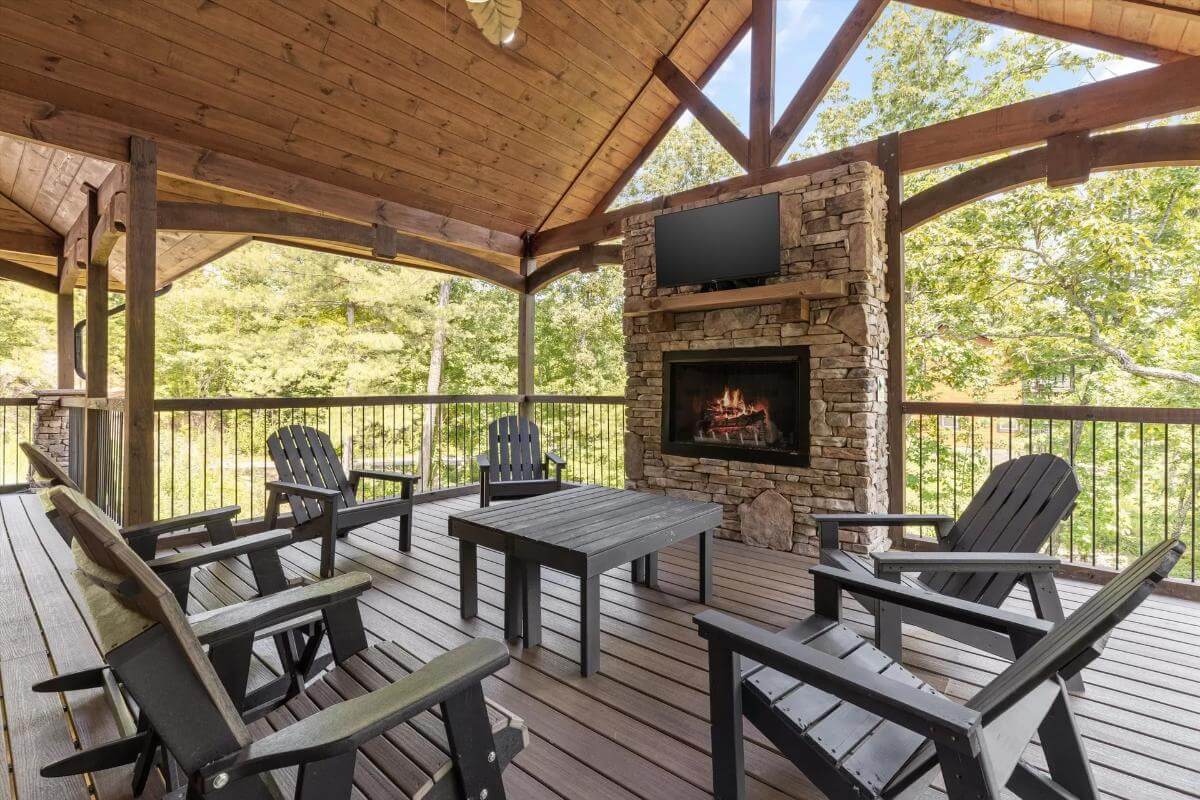 Covered porch with dark wood chairs, a matching table, and a stone fireplace with a TV on top.