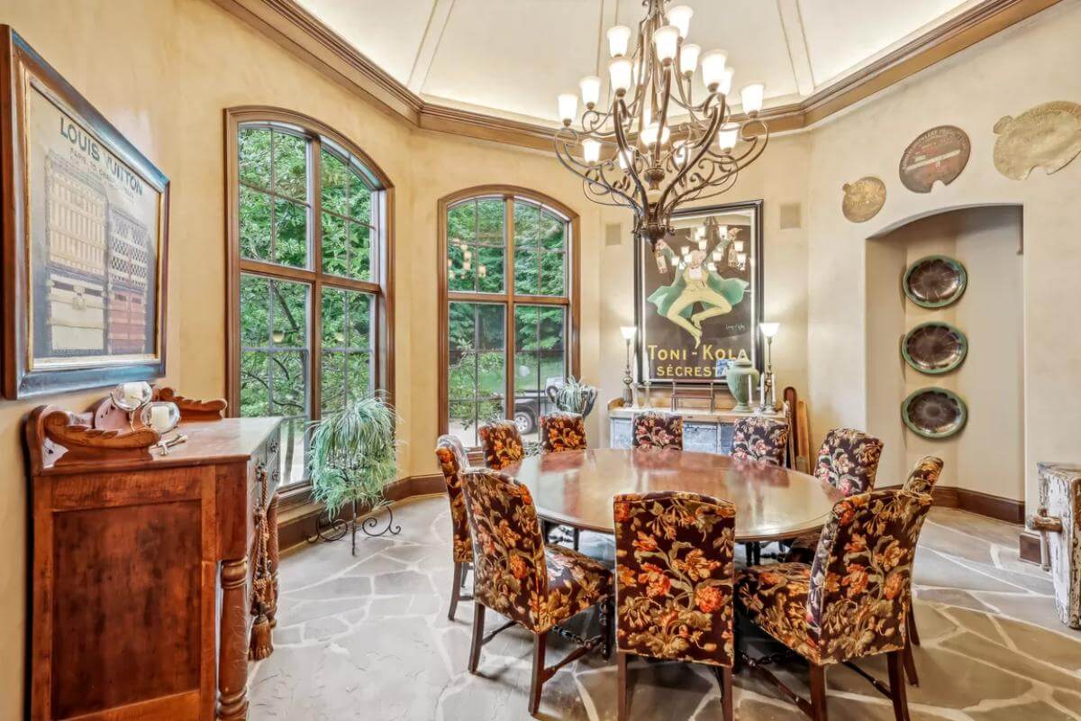 Dining room with a round dining set illuminated  by a grand chandelier and arched windows.