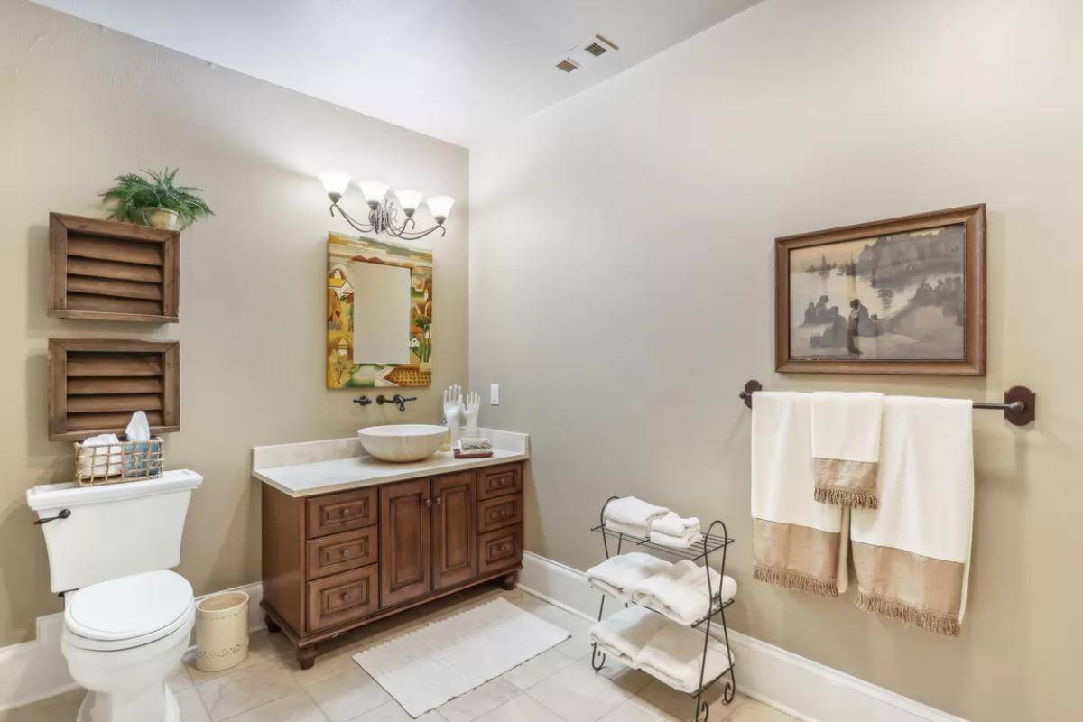 Bathroom with a vessel sink vanity and louvered cabinets fixed above the toilet.