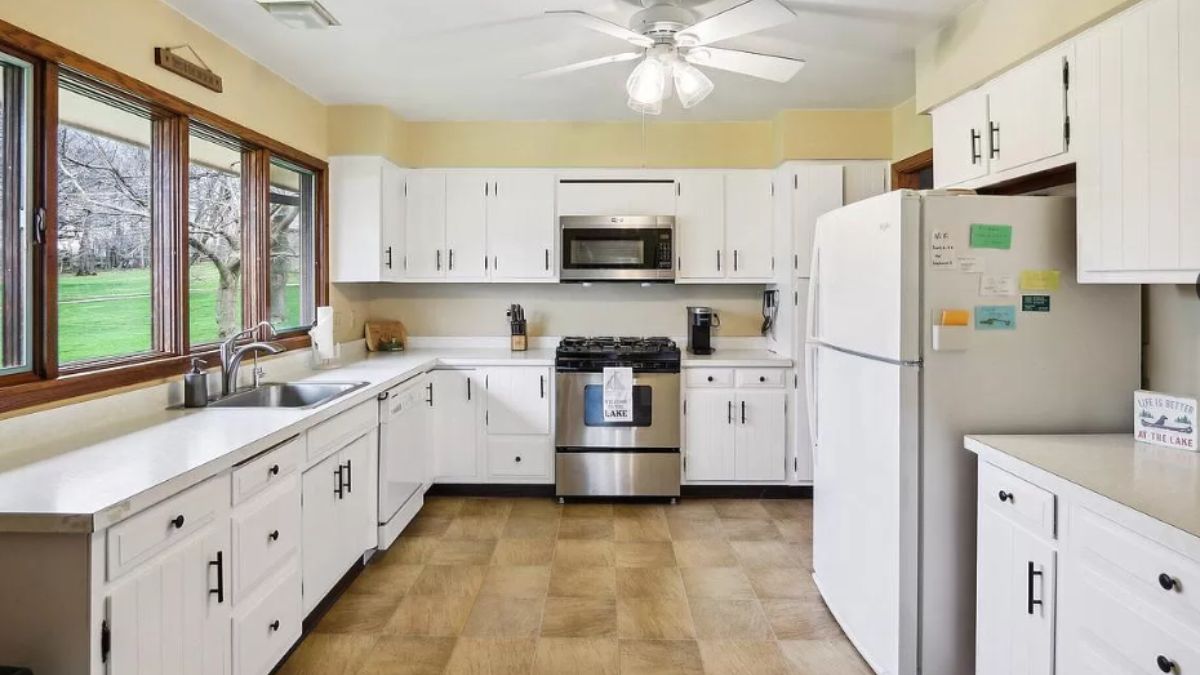 A kitchen with tiled floor, windows, countertops, cabinets, sink, and kitchen appliances.