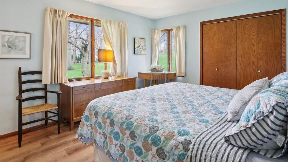 A bedroom with a bed, windows, a cabinet, a desk, and chairs.