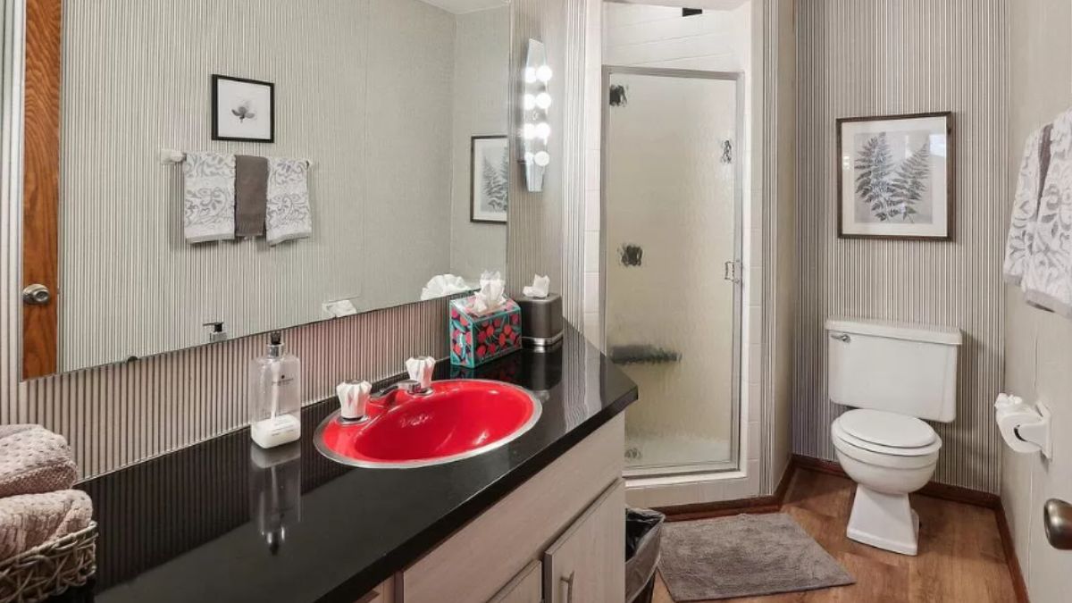 A bathroom with a vanity, mirror, toilet, and shower room.