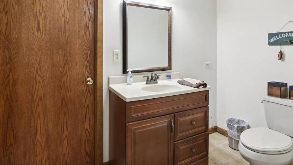 A bathroom with a vanity, cabinet, toilet and mirror.