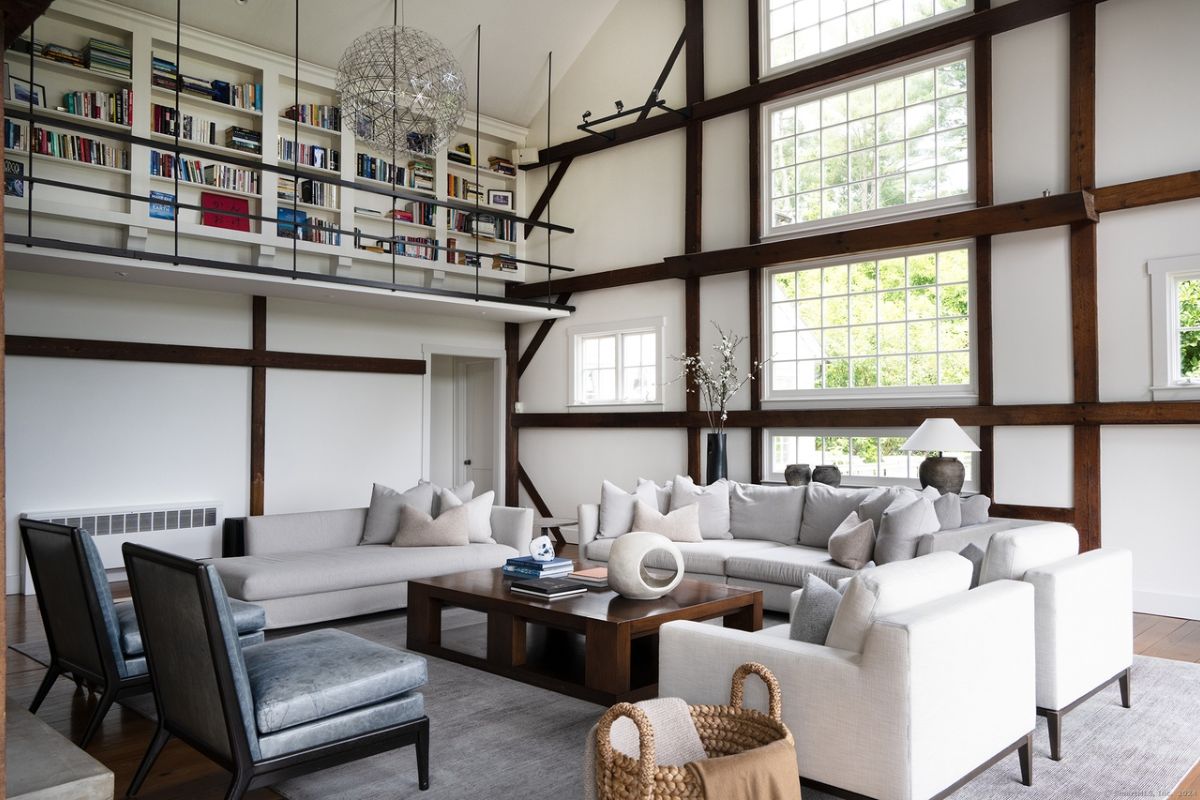 A living room with windows, white couches with pillows, chairs, and a center table.