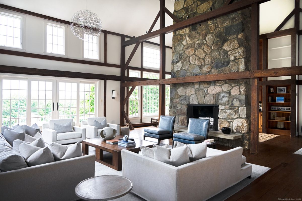 A living room with a stone fireplace, windows, white couches with pillows, chairs, and a center table.