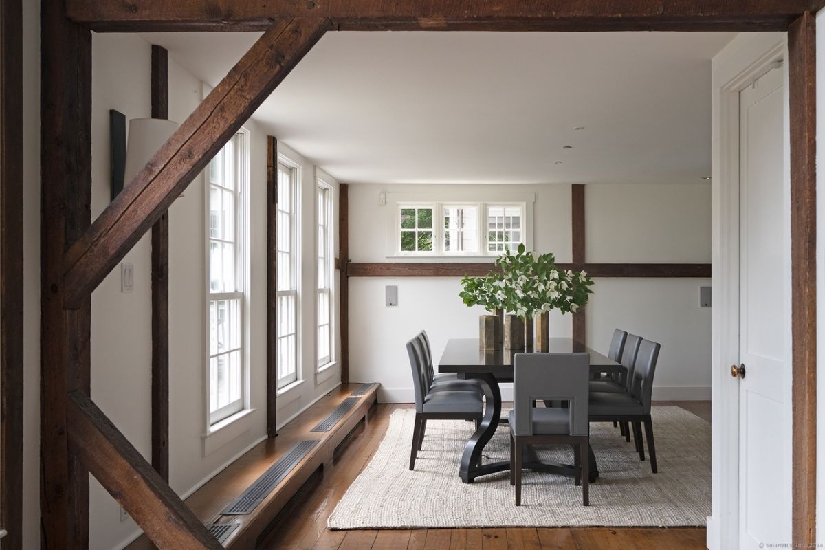 A dining room with windows, a rug, and a dining table surrounded by chairs.