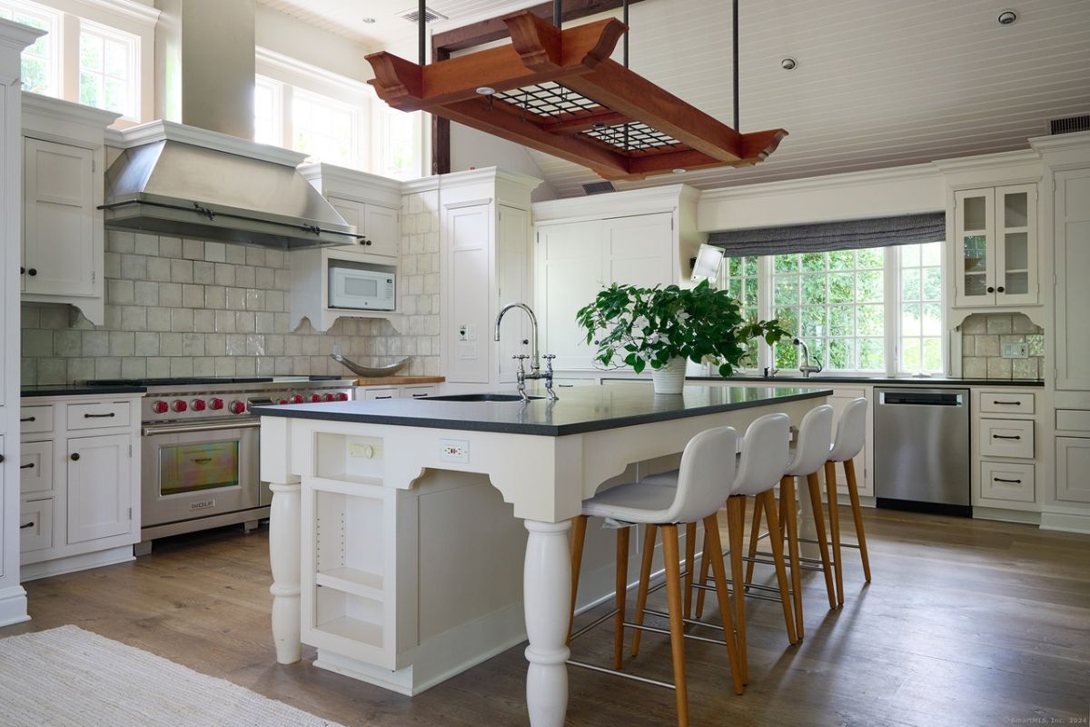 A kitchen with countertops, a sink, chairs, cabinets, and kitchen appliances.