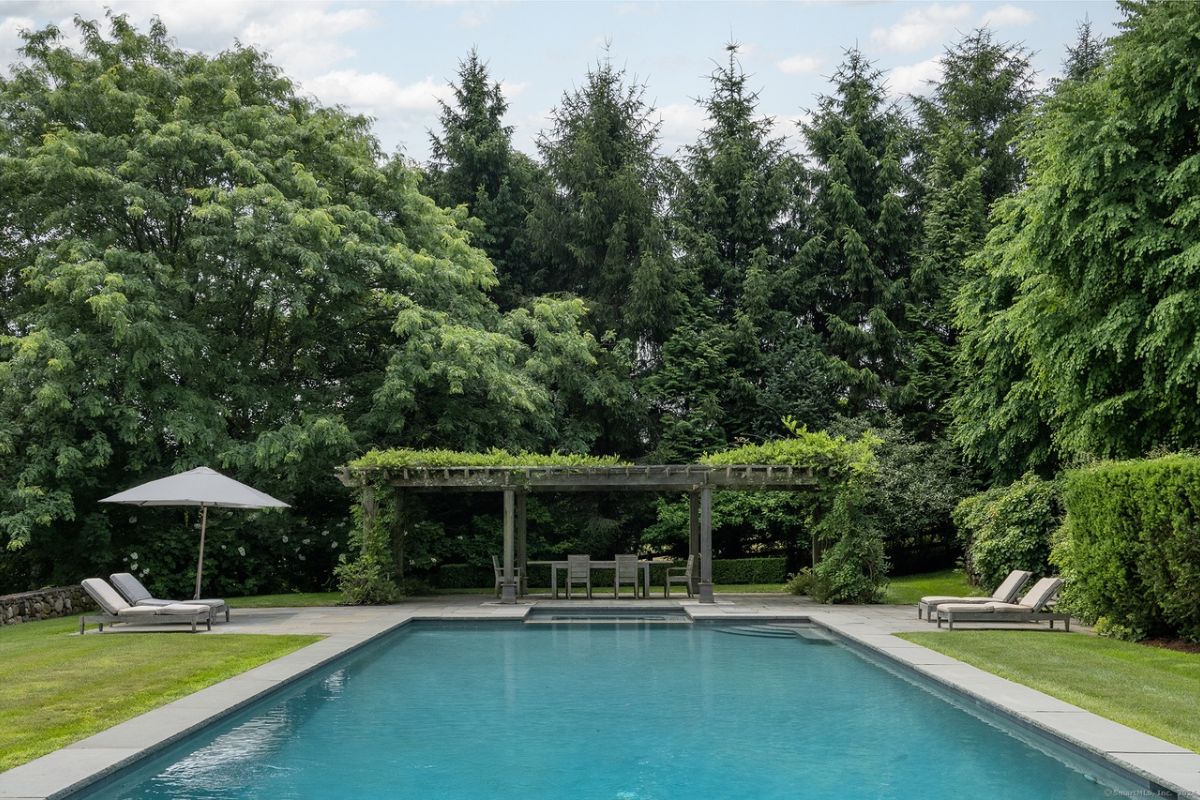 A swimming pool with chairs and umbrellas surrounded by trees.