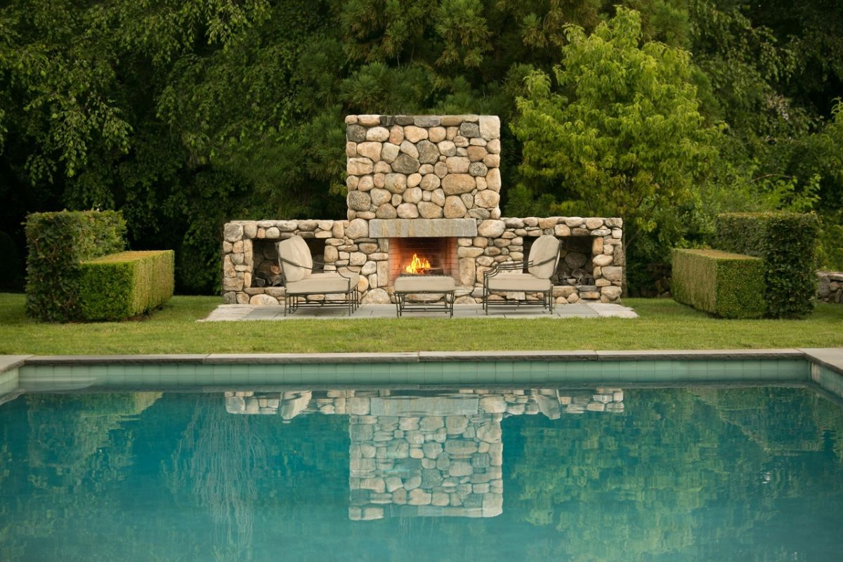 A swimming pool and stone fireplace surrounded by trees.