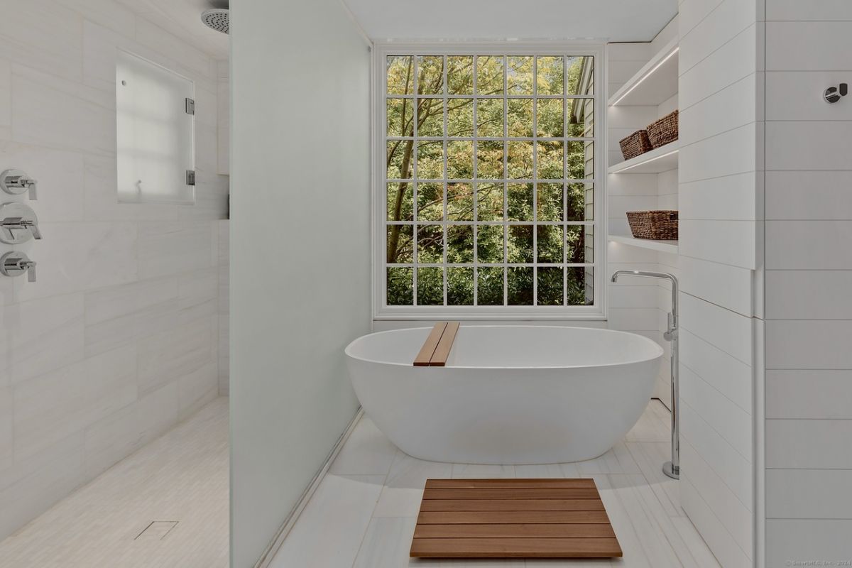 A bathroom with a window, tiled floor, and bathtub.