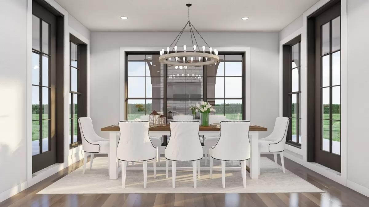 Dining room with an 8-seater dining set illuminated by a round chandelier and surrounding windows.