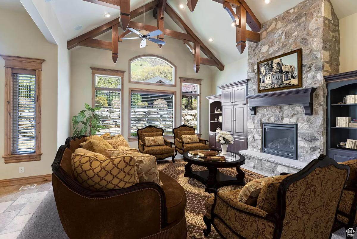 Living room with a stone fireplace, traditional chairs, and a cathedral ceiling adorned by decorative trusses.