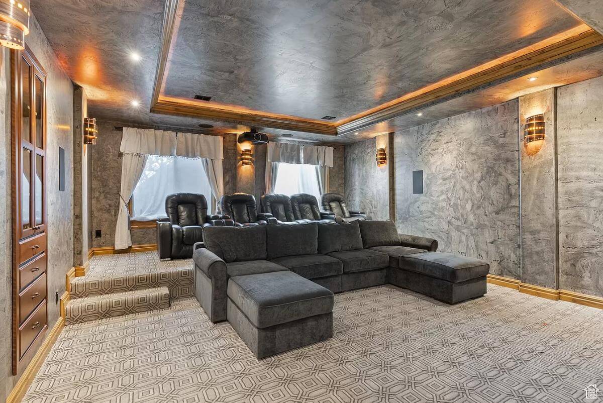 Theater with leather recliners, a black sofa, and a tray ceiling highlighted by warm coved lighting.