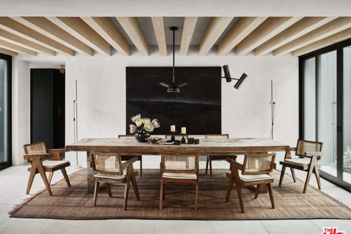 A dining room with an exposed beam ceiling, painting, rug, and a dining table surrounded by chairs.