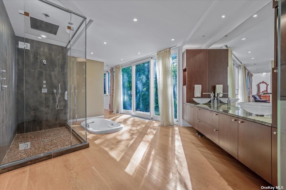 A bathroom with dual vanity, mirror, cabinets, bathtub, and shower room.