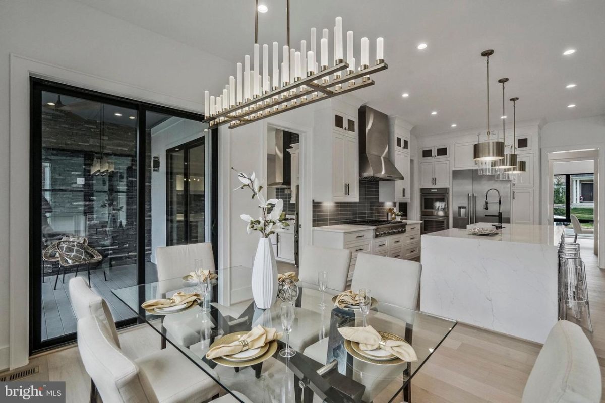 A dining room with a chandelier and a glass dining table surrounded by chairs.