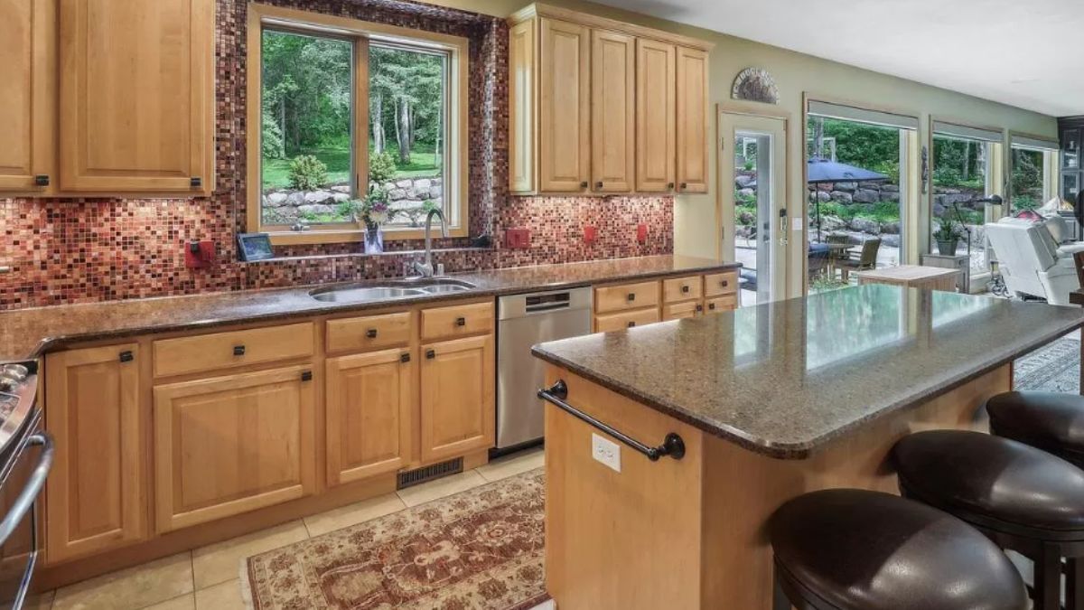 A kitchen with an island, stools, rug, countertop, sink, stove, and cabinets.