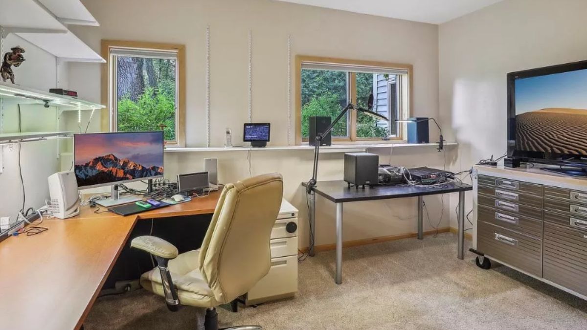 A home office with windows, a desk, a chair, a cabinet, and a TV.