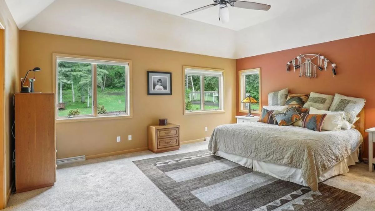 A bedroom with a bed, windows, a ceiling fan, cabinets, and a rug.