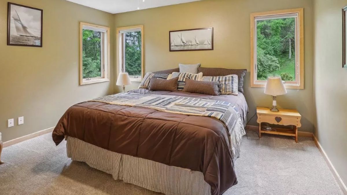 A bedroom with windows, a nightstand, and a lampshade.