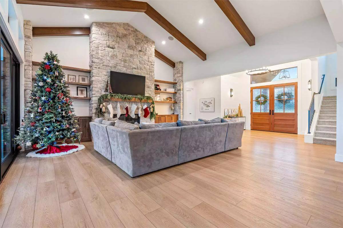 Great room with a stone fireplace, an L-shaped sectional, and a vaulted ceiling lined with exposed beams.