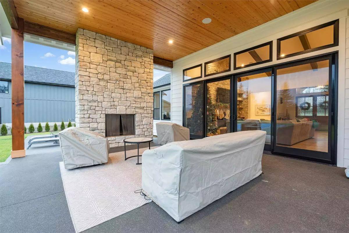 Covered porch with a stone fireplace and a wood-paneled ceiling.