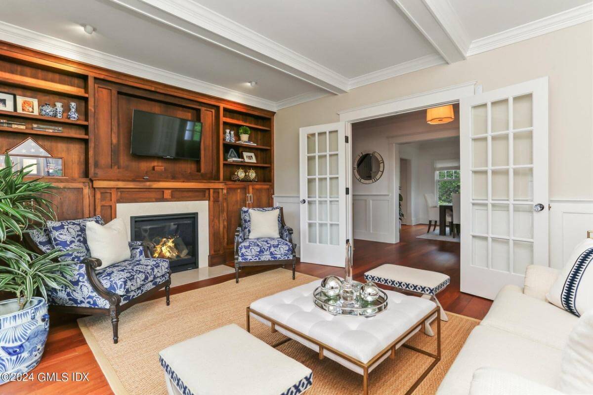 Living room with a French door, patterned chairs, a sectional sofa, and a fireplce topped by a TV.