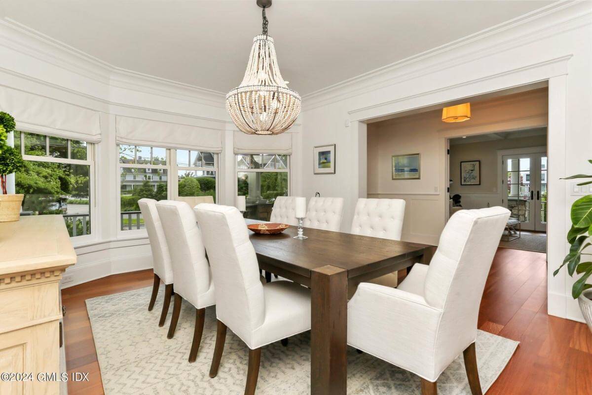 Dining room with a bay window and a dark wood dining set illuminated by a beaded chandelier.