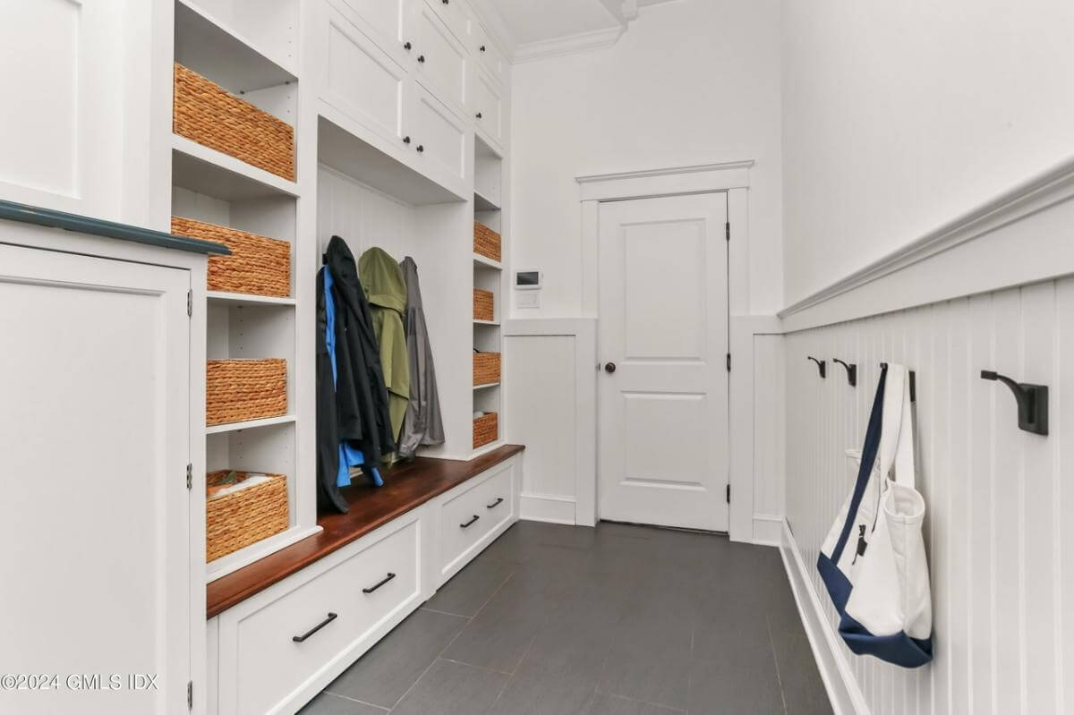 Mudroom with built-in shelves, white cabinets, coat hooks, and a bench.