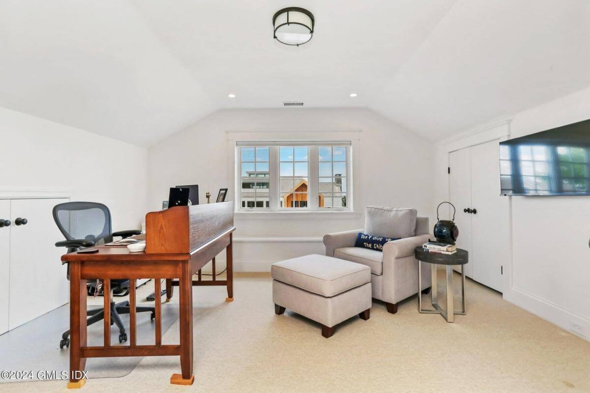 Office with a dark wood desk, a lounge chair, and a wall-mounted TV under a coved ceiling.