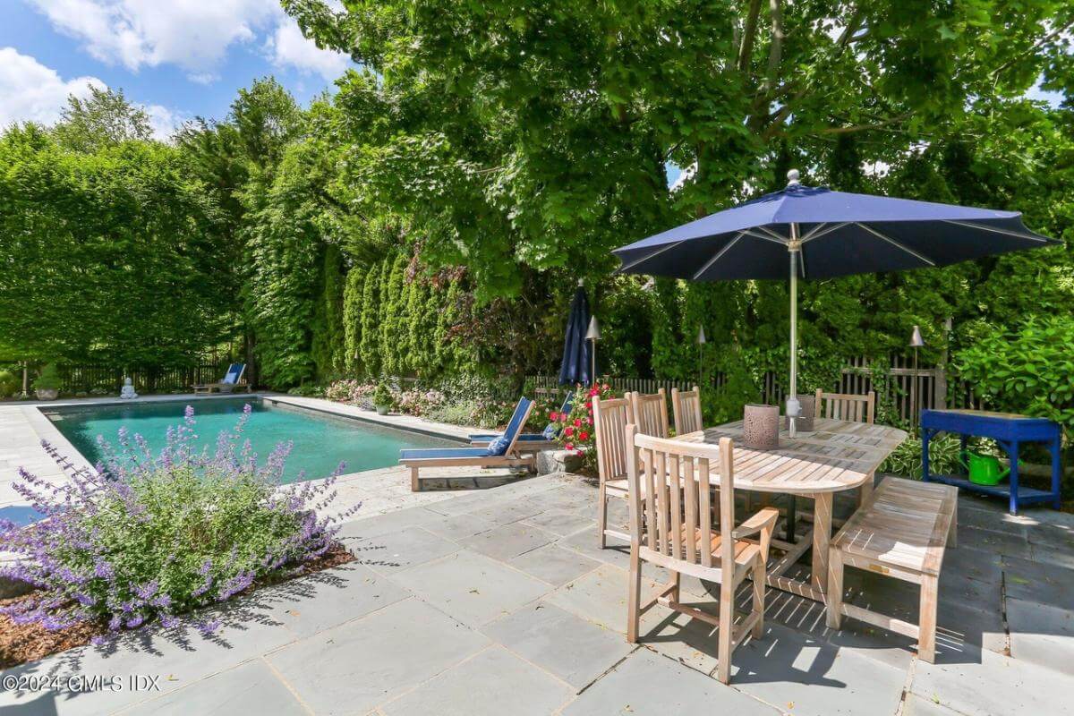 Outdoor dining with an wooden chairs, a matching bench, and an oval table topped by an umbrella.