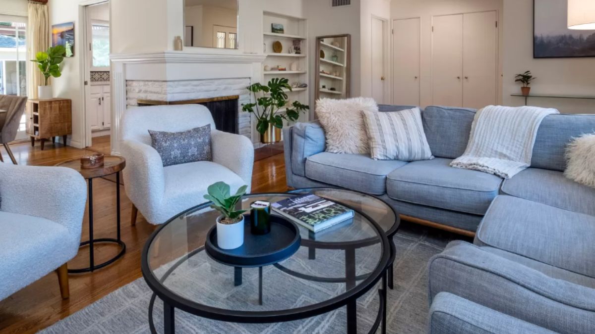 A living room with chairs, couches, a rug, and a glass center table.