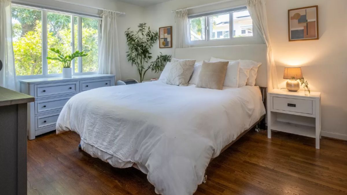 A bedroom with a bed, nightstands, paintings, a window, and a cabinet.