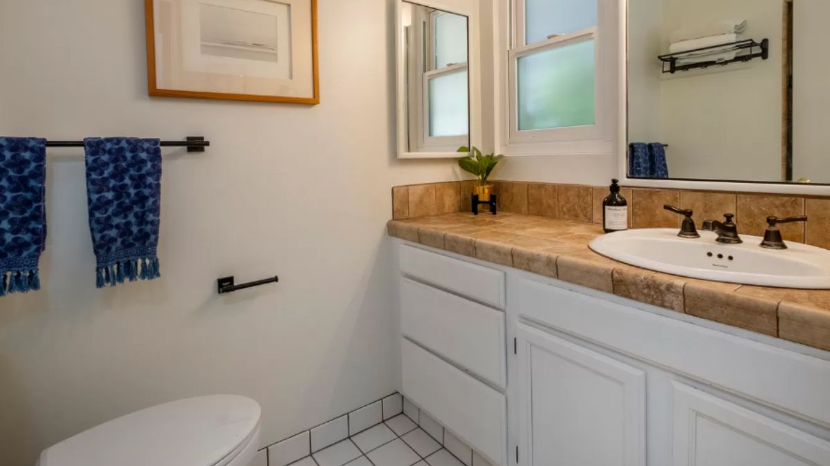 A bathroom with a vanity, mirror, cabinets, and a toilet.