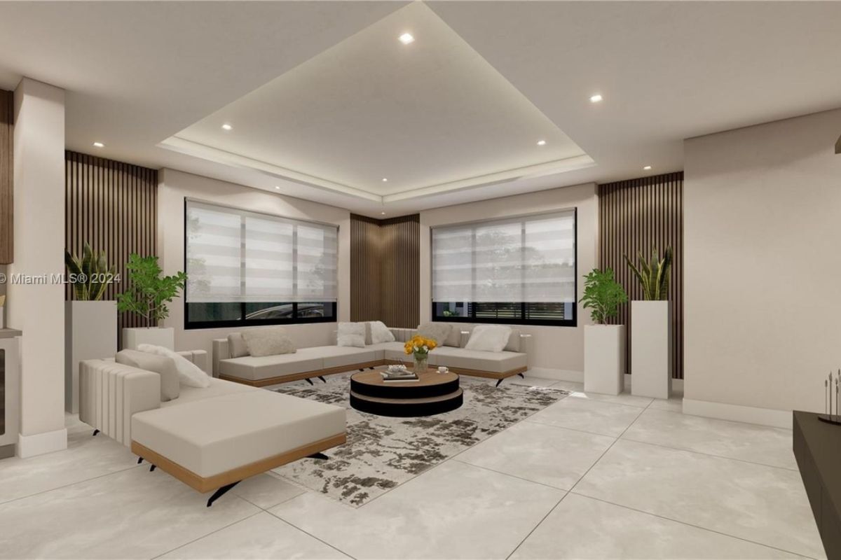 A living room with windows, houseplants, white couches, a rug, and a round center table.