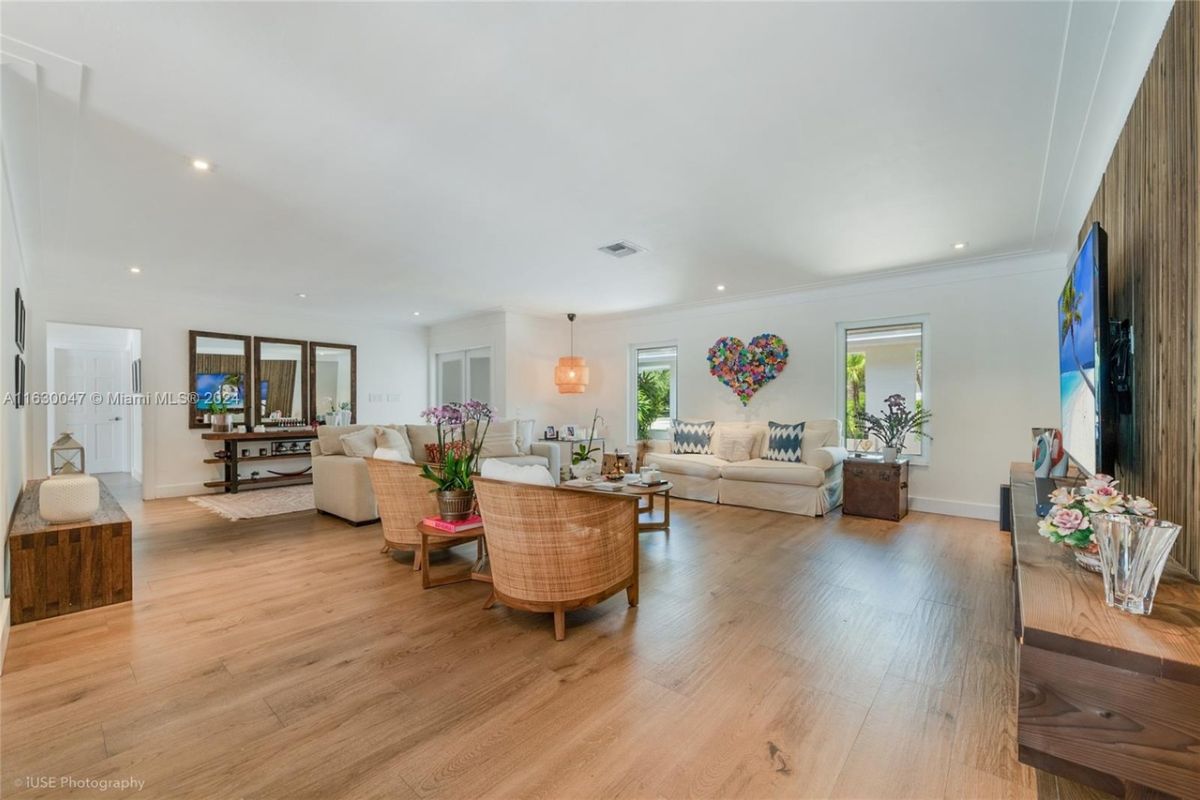 A living room with a TV, couches, cabinets, chairs, a center table, and a mirror.