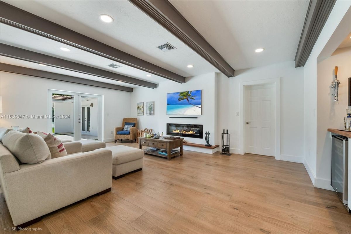 A living room with an exposed beam ceiling, a TV, a fireplace, a chair, couches, and a center table.