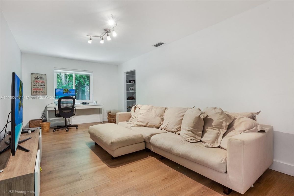 A living room with a window, a desk with a computer, a couch, and a TV.