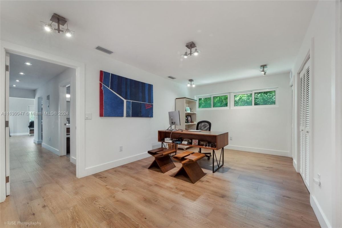 A home office with a wooden floor, windows, a painting, and a desk with an office chair.