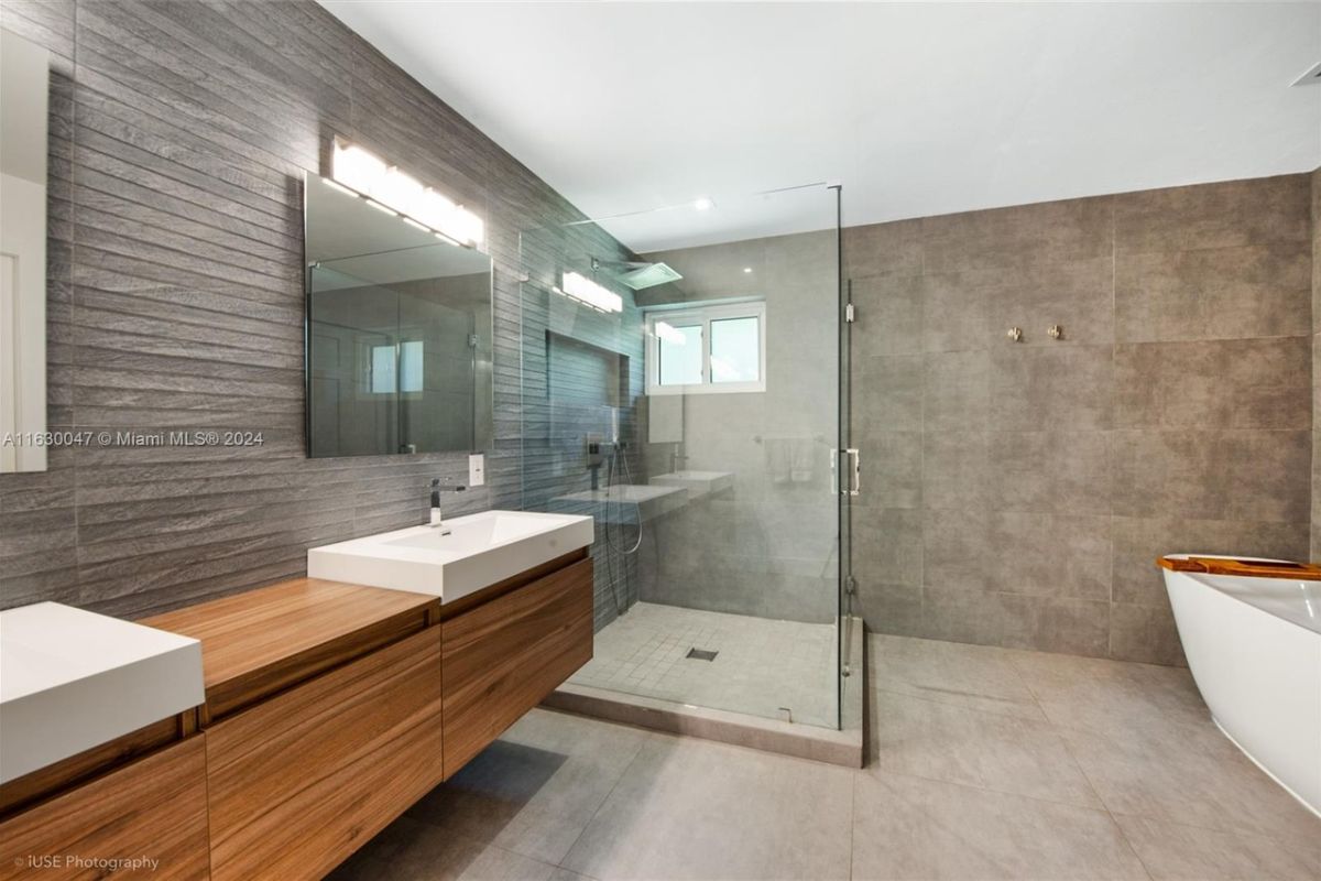 A bathroom with a dual vanity, mirrors, a bathtub, and a shower room.